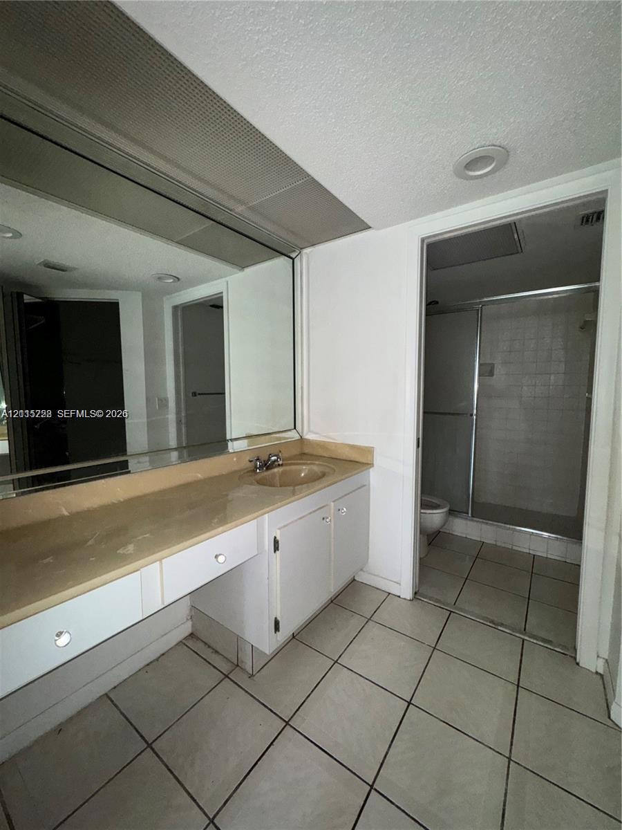 Bathroom featuring a vanity with an integrated sink, expansive wall-mounted mirror, ceramic tile flooring, and a walk-in shower enclosure