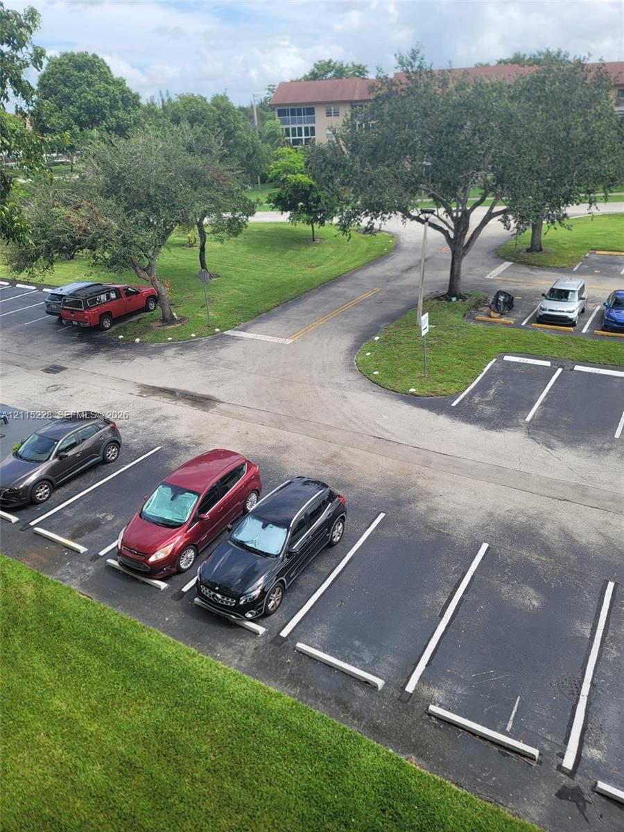 Asphalt parking area with designated stalls, mature trees, and landscaped green space