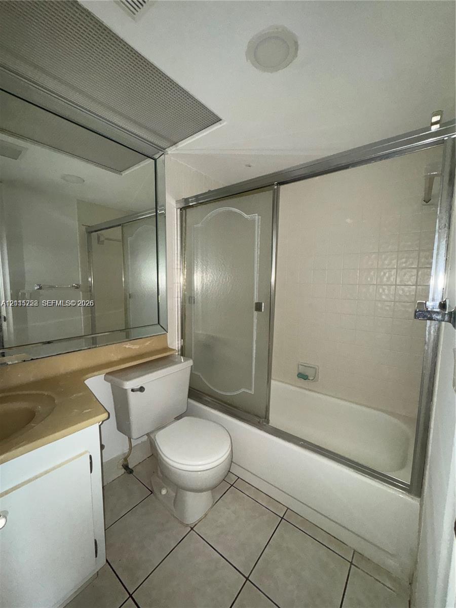 Bathroom featuring tile flooring, a built-in vanity with an integrated sink, a large wall-mounted mirror, and a tub-shower combination with sliding glass doors