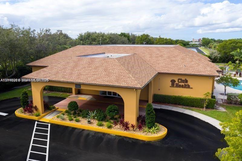 Exterior perspective of the facility featuring a covered porte-cochre, a shingled hipped roof, paved circular driveway, and curated perimeter landscaping