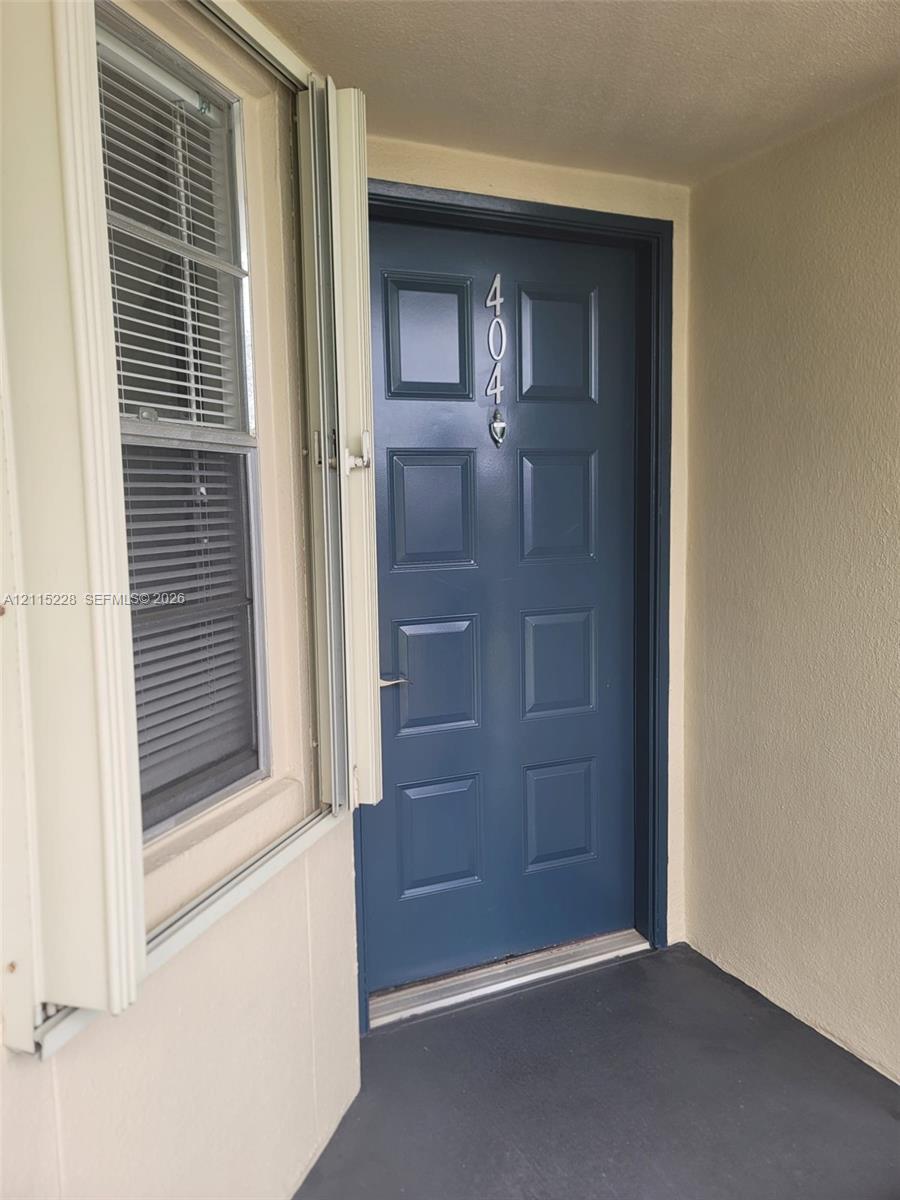 Blue paneled door featuring metallic house numbers and a silver-finish handle set, paired with a vertical-slider window with integrated mini-blinds