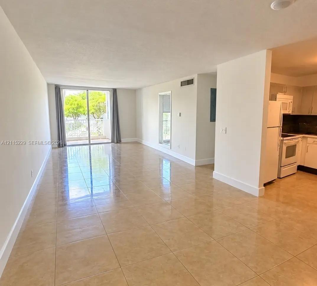 Open-concept area featuring oversized ceramic tile flooring, sliding glass door access to a balcony, and white cabinetry with built-in appliances
