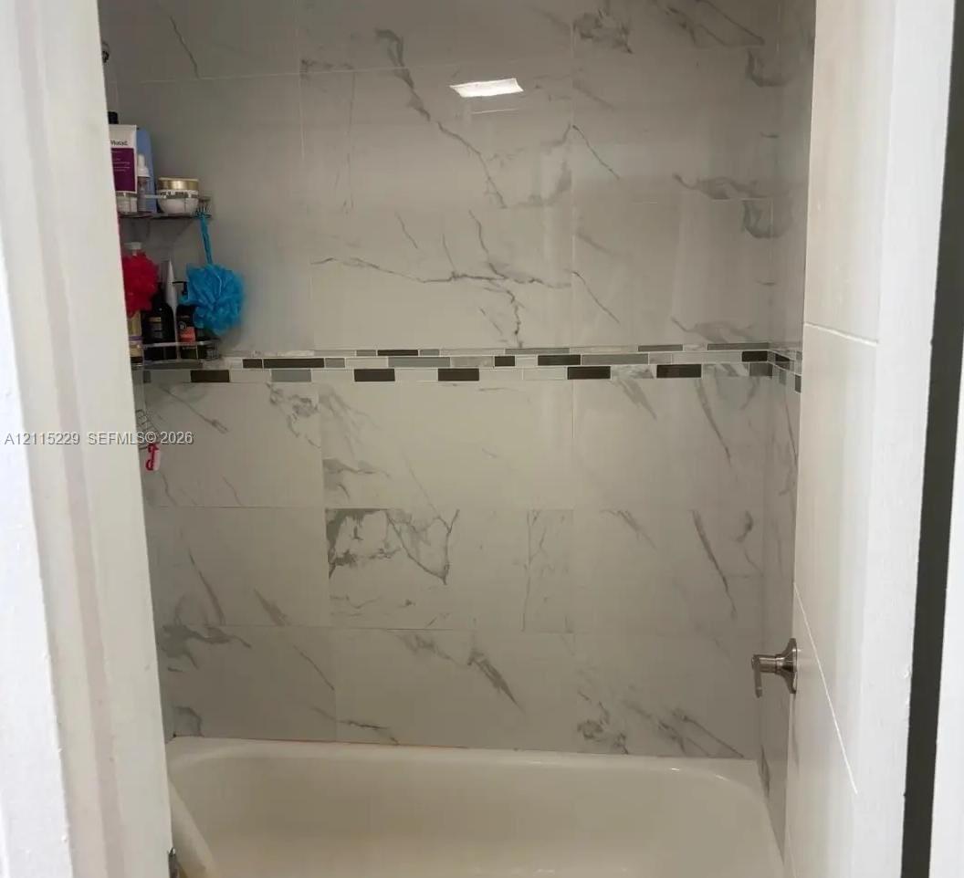 Full-height wall tiling with a vein-patterned finish, complemented by a horizontal decorative mosaic tile border and a standard bathtub fixture