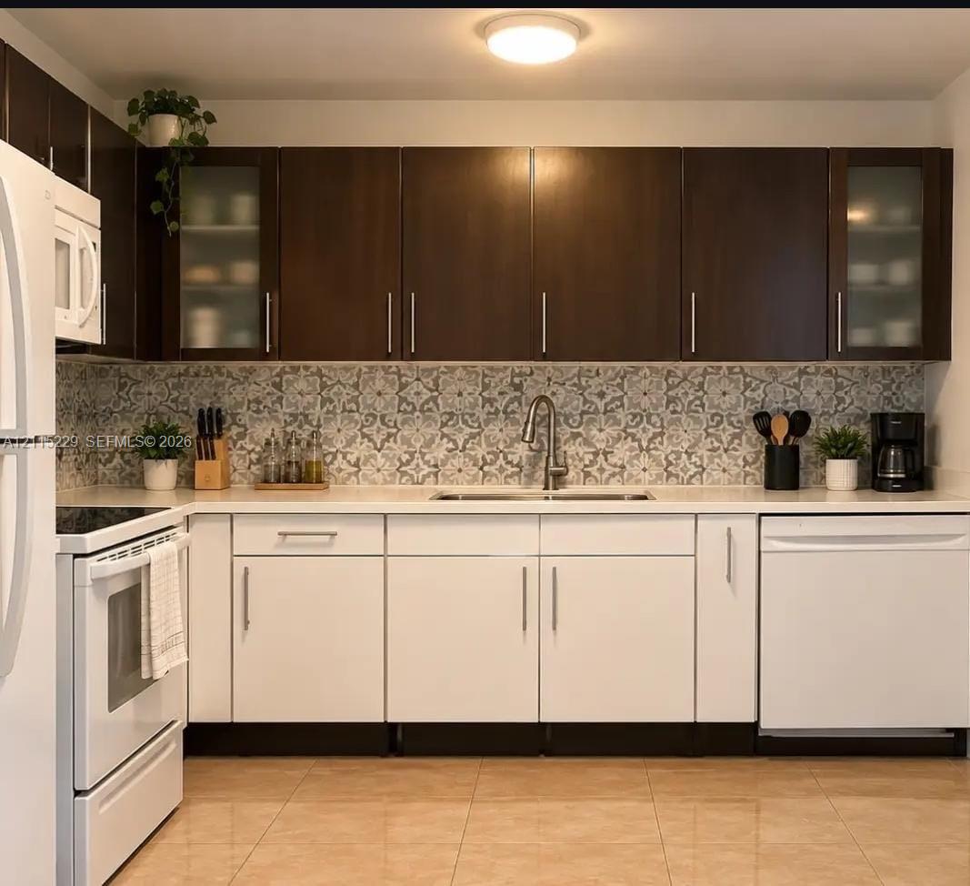 Kitchen featuring two-tone cabinetry with upper glass-panel accents, solid surface countertops, patterned tile backsplash, and stainless steel undermount sink with arched faucet