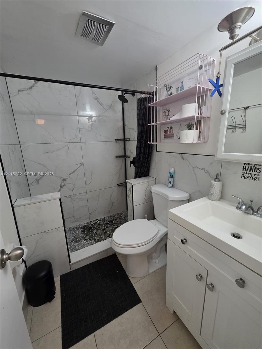 Walk-in shower featuring large-format tile surround, river stone flooring, and matte black frame