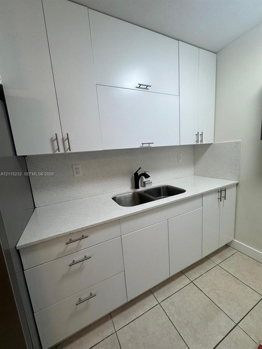 Flat-panel white cabinetry featuring stainless steel bar pulls, stone-composite countertop, matching full-height backsplash, undermount double-basin stainless steel sink, and matte black high-arc faucet