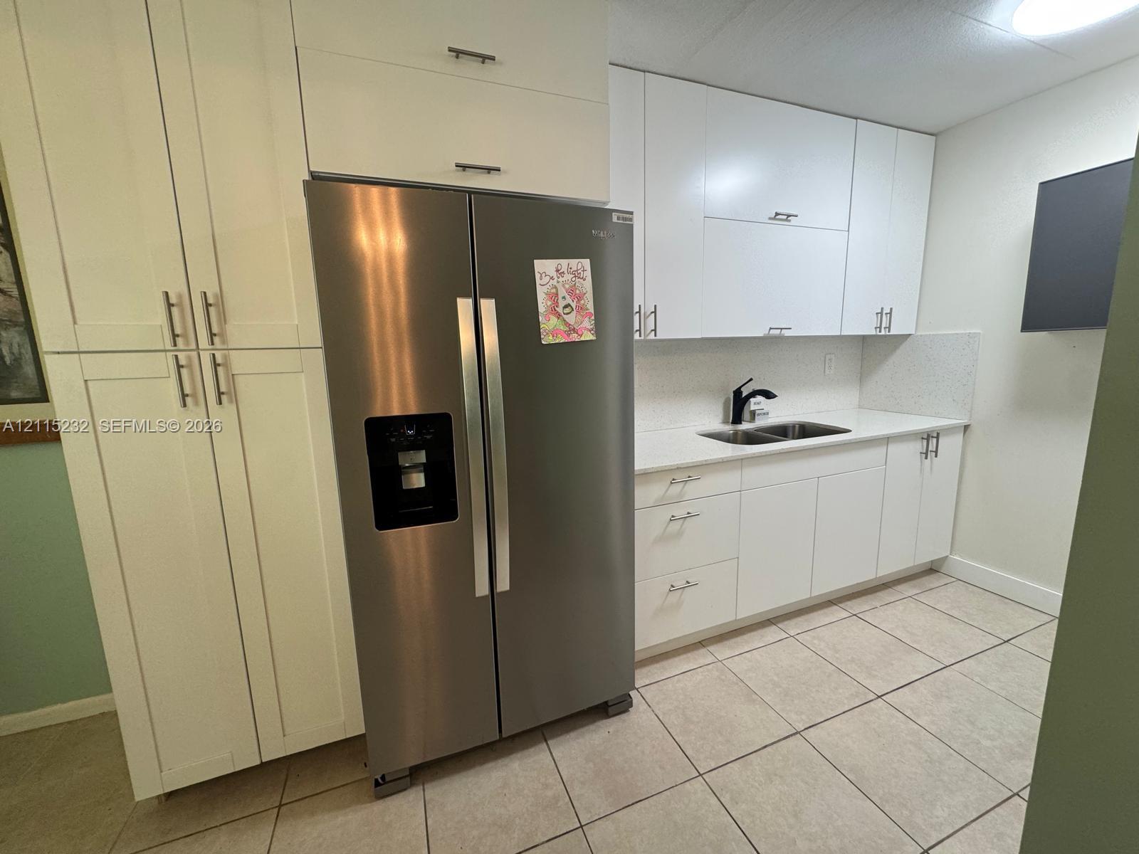 Kitchen featuring white shaker-style cabinetry, a stainless steel side-by-side refrigerator, solid-surface countertops, dual-basin stainless steel sink with matte black faucet, and tiled flooring