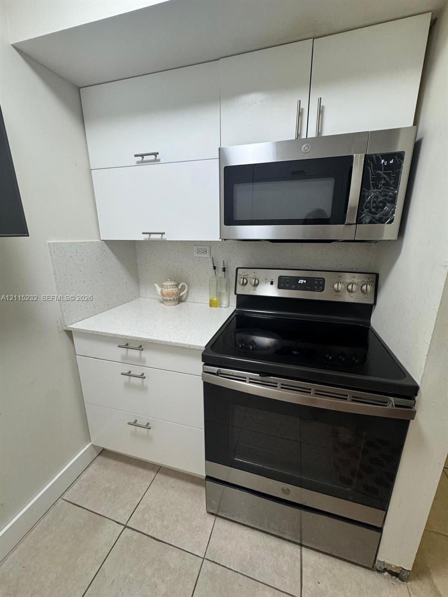 White flat-panel cabinetry featuring brushed nickel pulls, stone-composite countertops, and a built-in stainless steel microwave and range