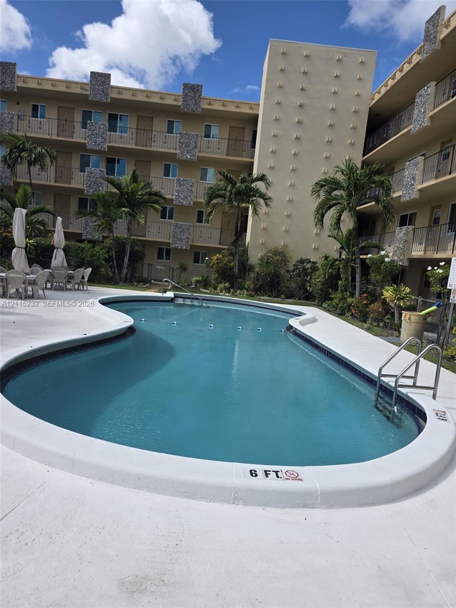 Curved swimming pool featuring a concrete deck, metal handrails, and mature palm trees