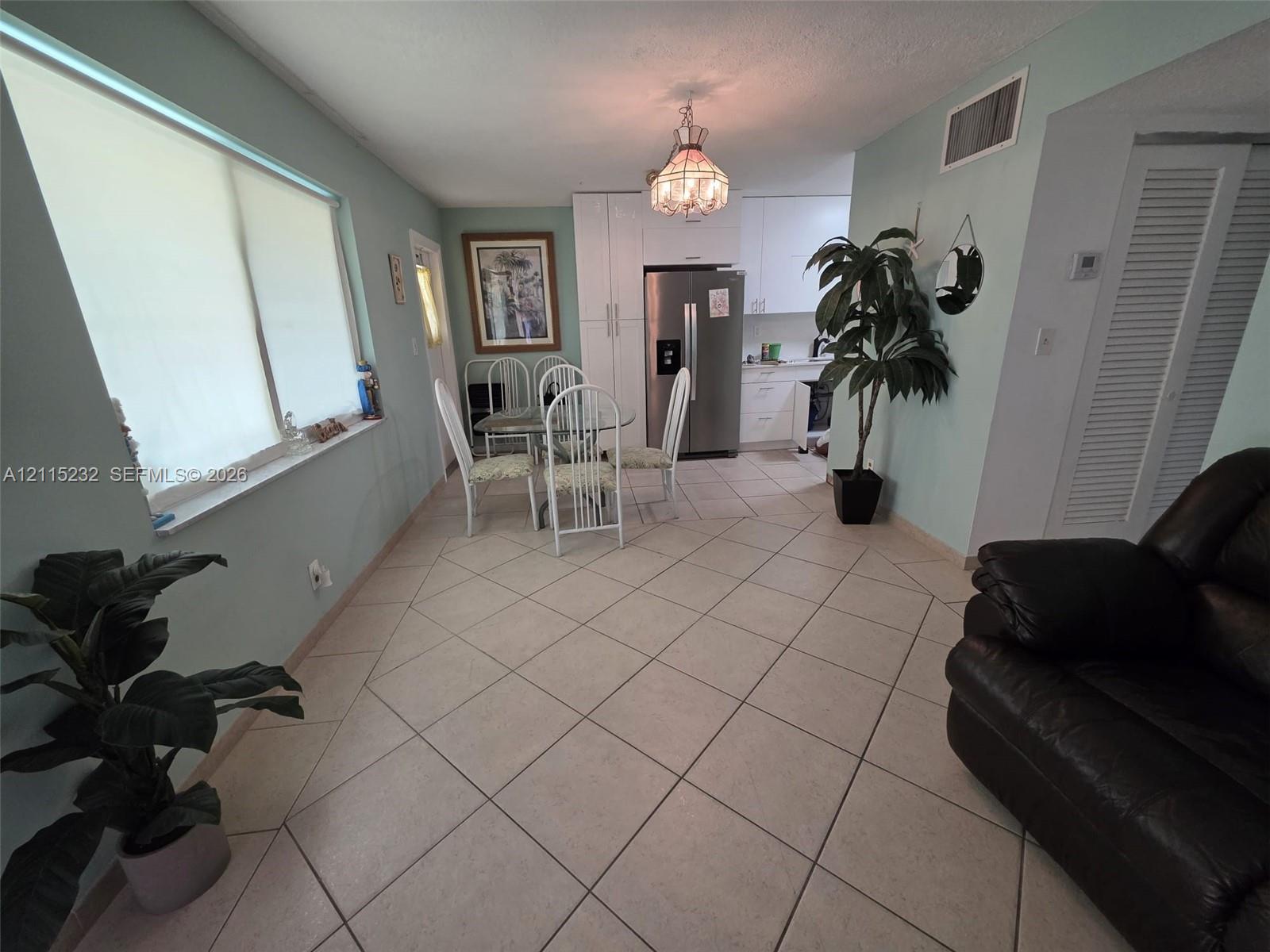 Ceramic tile flooring, built-in floor-to-ceiling cabinetry, stainless steel refrigerator, and a decorative pendant chandelier