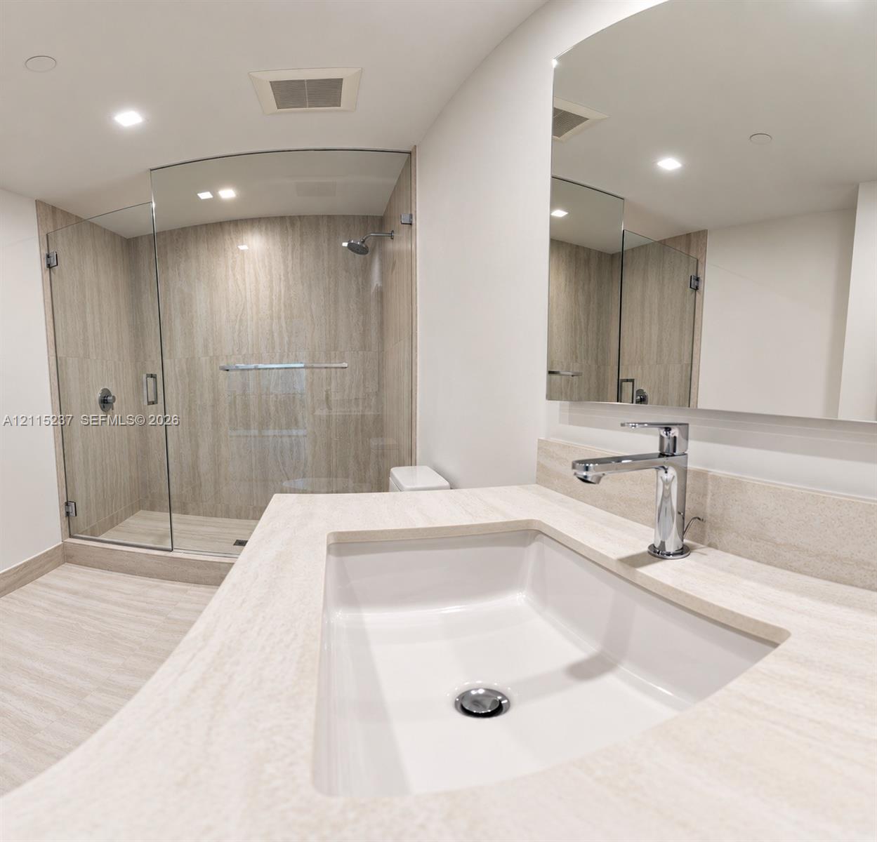 Bathroom featuring a vanity with an integrated rectangular sink and polished chrome faucet, stone-finish countertop, frameless glass shower enclosure, and stone-finish wall tile