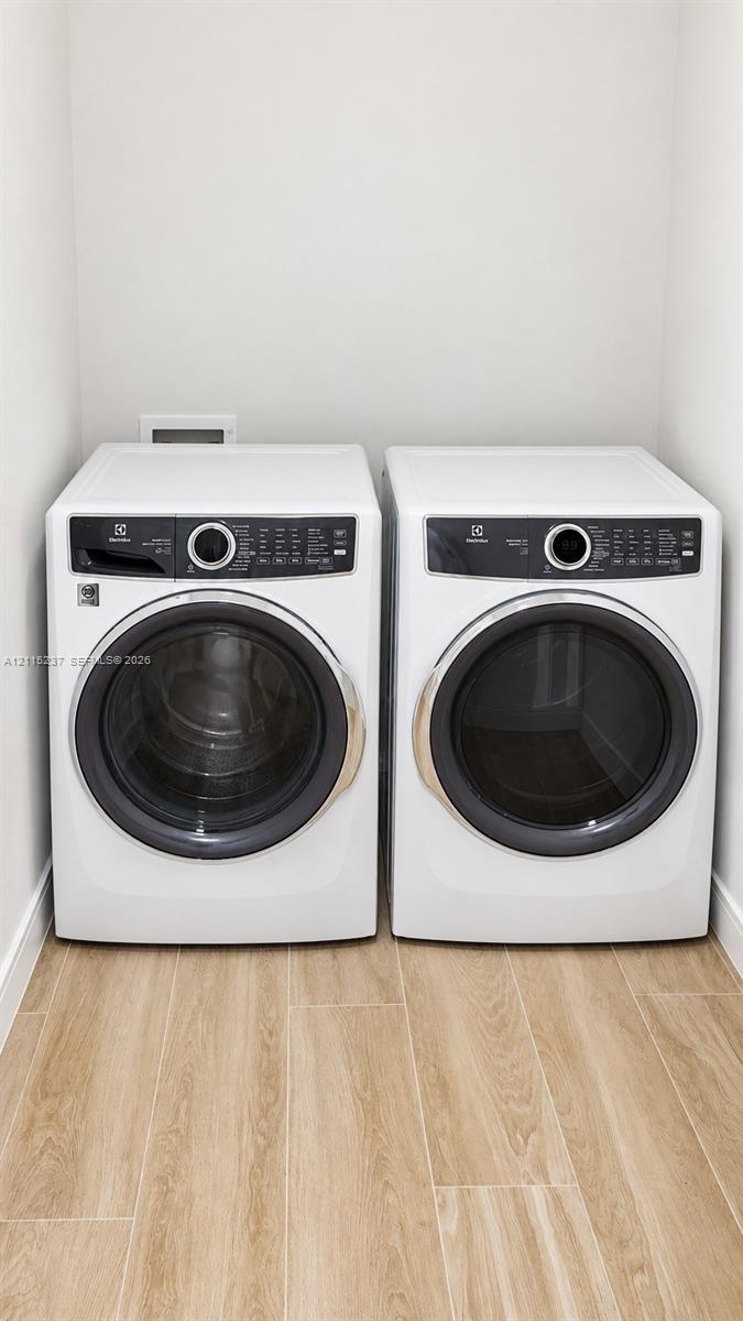 Laundry area featuring front-loading washer and dryer units set upon wood-finish flooring