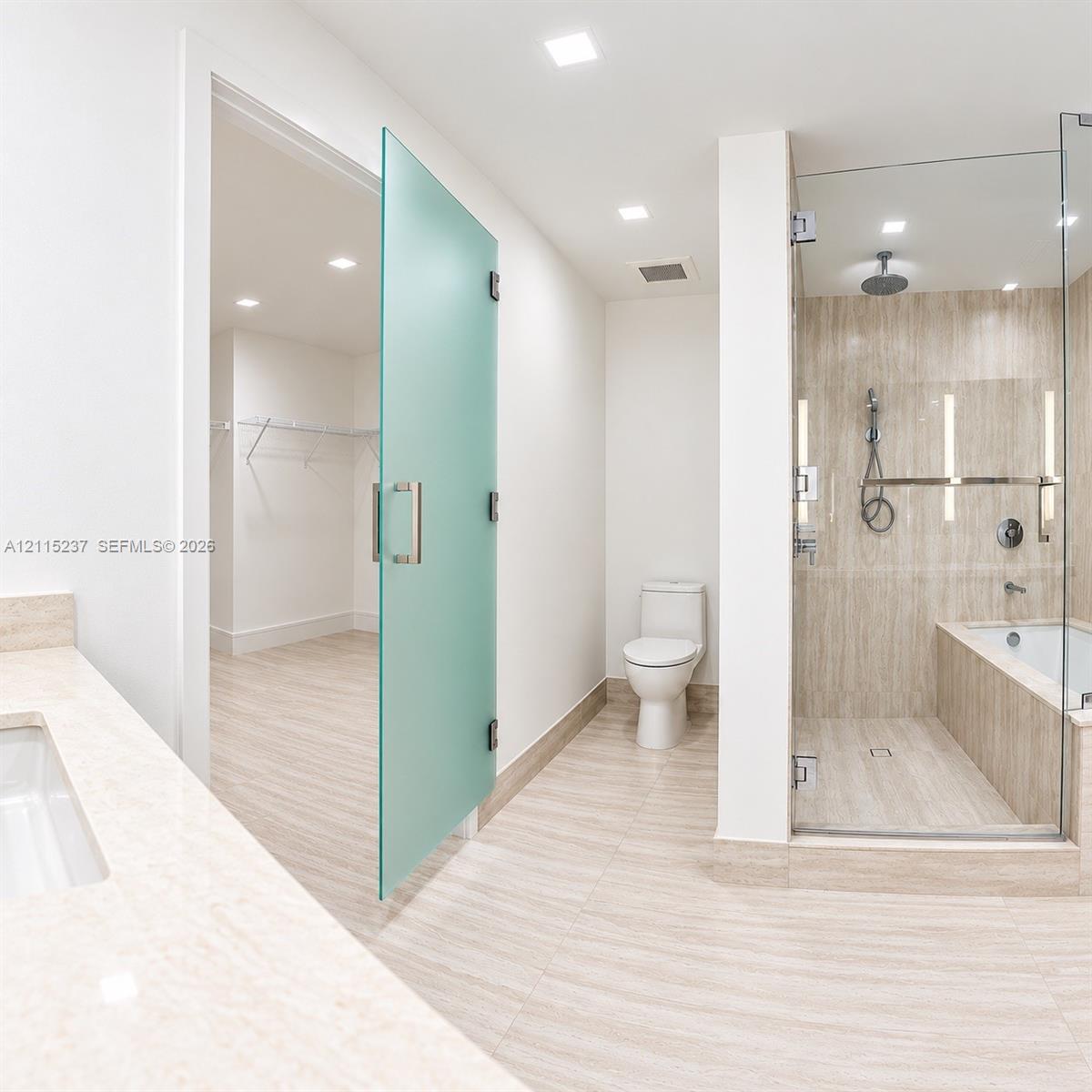 Bathroom featuring stone-finish floor and wall tiles, glass-enclosed shower with integrated tub, frosted glass door, and neutral-toned countertop with an undermount sink