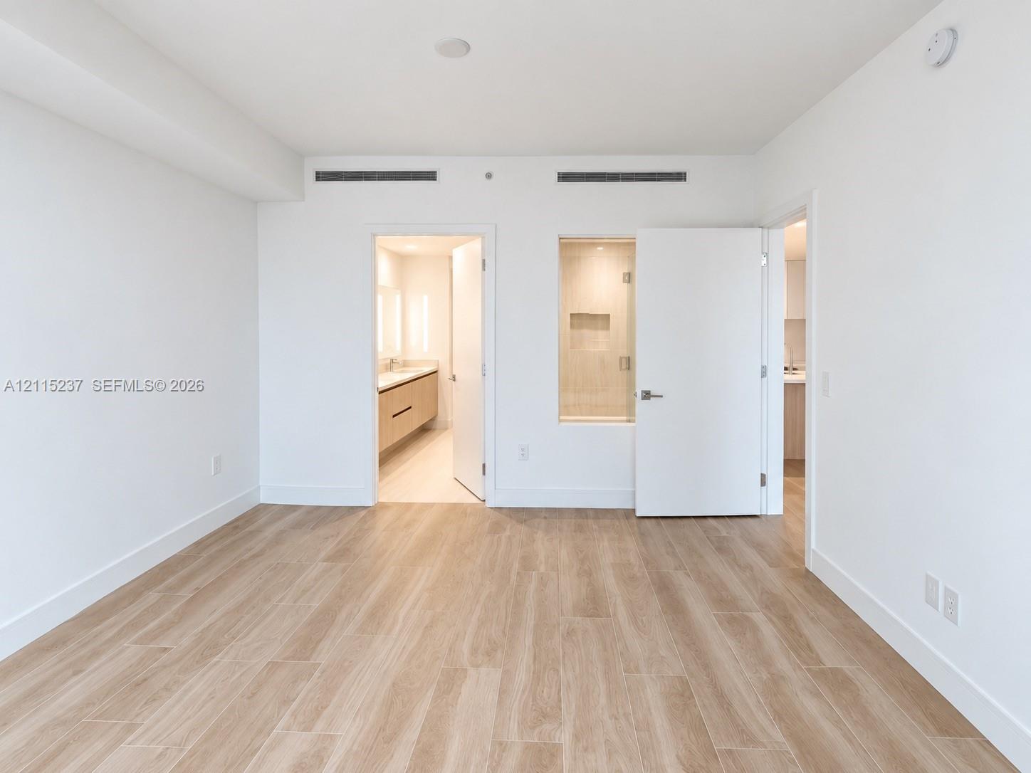 Interior space featuring light-toned wood-finish flooring, white walls, minimalist door hardware, and a fixed glass window panel