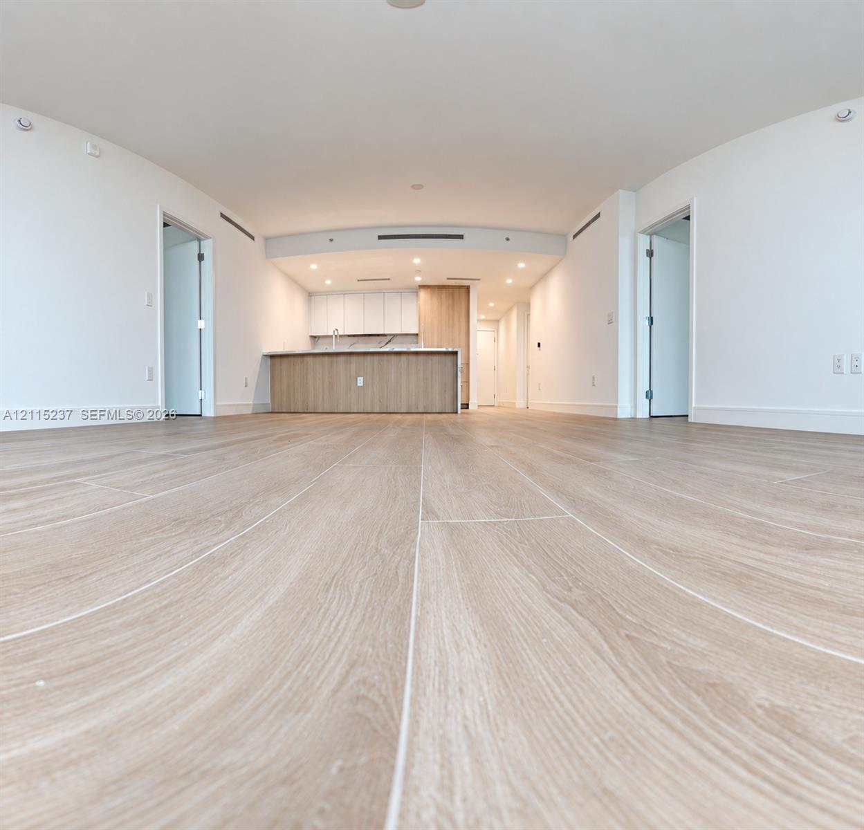 Open-concept interior featuring light wood-finish flooring, recessed lighting, and a kitchen island with stone-finish countertops and wood-grain cabinetry