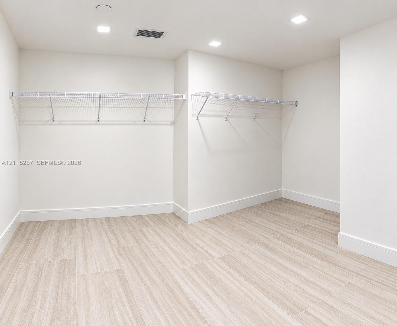 Walk-in storage space featuring wood-finish flooring, white walls, and built-in white wire shelving with integrated lighting