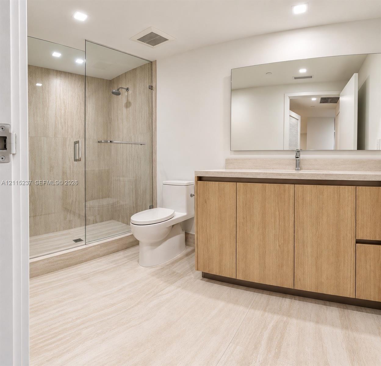 Bathroom featuring a glass-enclosed walk-in shower with tile surround, wood-finish cabinetry, stone-surface countertop, and a wide-format wall mirror