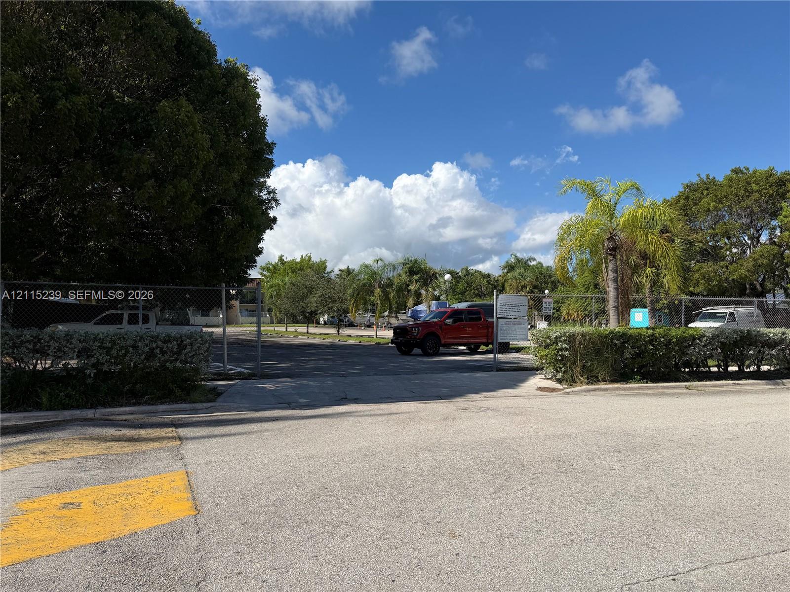 Paved lot featuring a chain-link perimeter fence, gated entrance, and mature landscaping