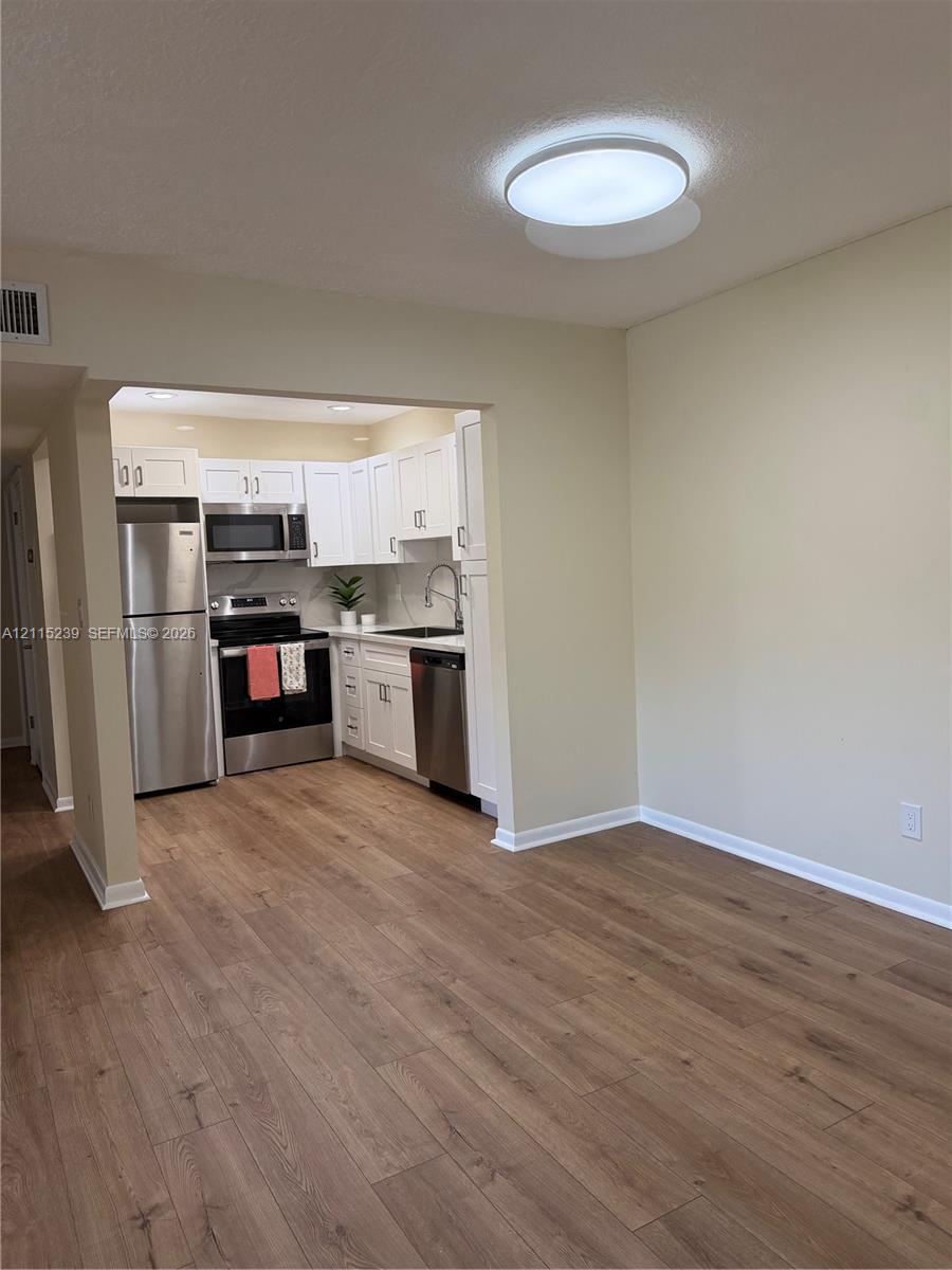 Kitchen featuring white shaker-style cabinetry, stainless steel appliances, and wood-finish flooring throughout