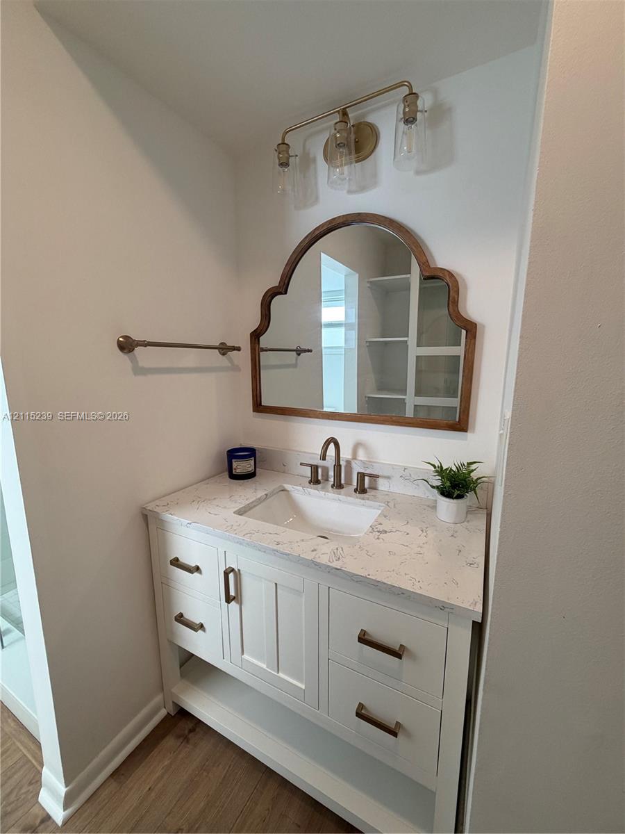 White vanity with stone-look countertop, undermount sink, brass-finish hardware, three-light wall-mounted fixture, and arched decorative mirror
