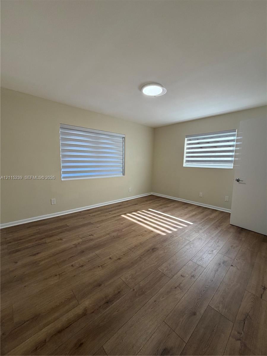 Room featuring wood-finish flooring, dual windows with fitted shades, and a flush-mount ceiling light fixture