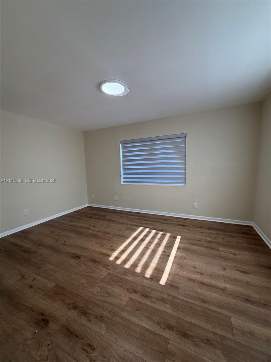 Neutral interior space featuring wood-finish flooring, a flush-mount ceiling light fixture, and a window with installed roller shades