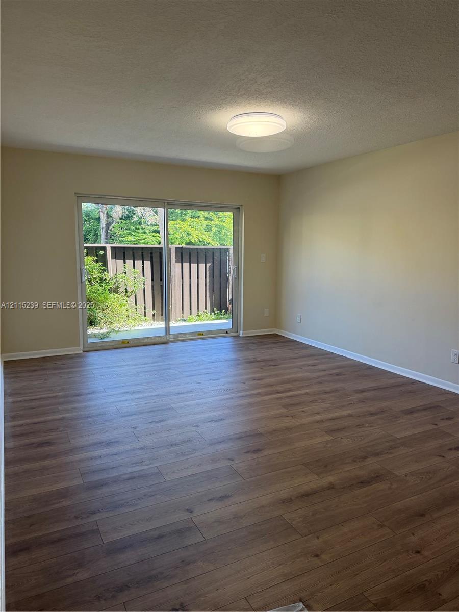 Room interior featuring wood-finish flooring, neutral wall paint, and a sliding glass door with a metal frame Room interior featuring wood-finish flooring, neutral wall paint, and a sliding glass door with a metal frame