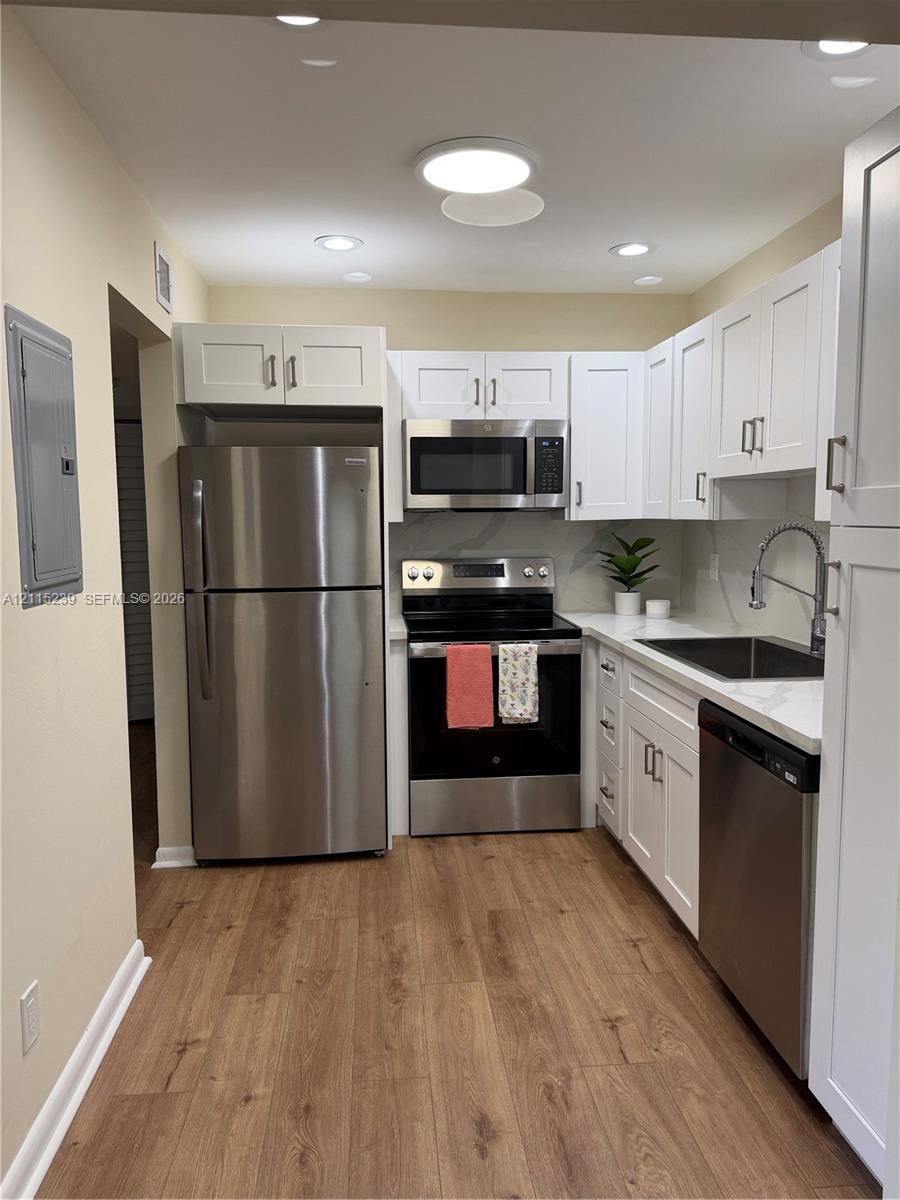 Kitchen featuring white shaker-style cabinetry, stainless steel appliances, wood-finish flooring, quartz countertops, and a gooseneck faucet