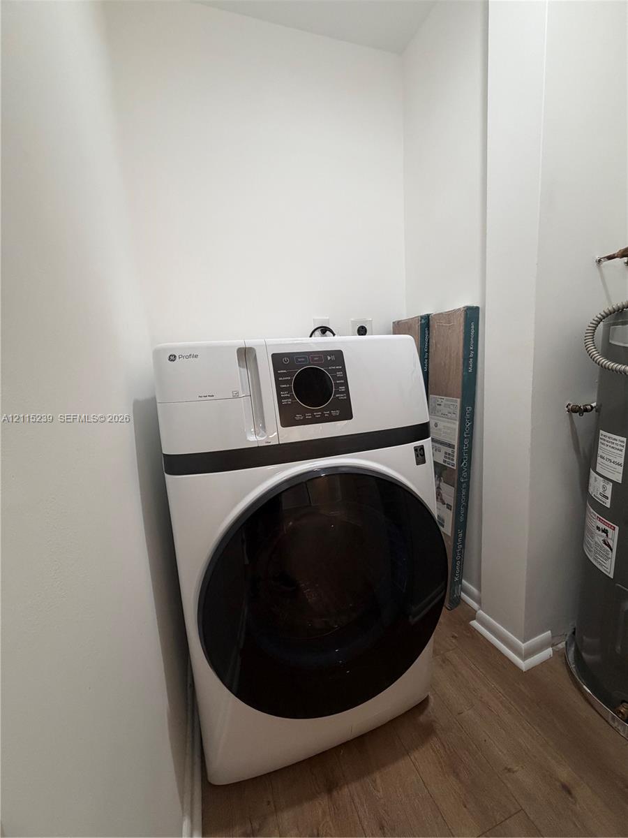 Utility area featuring a white front-load washer, wood-finish flooring, and a dedicated water heater