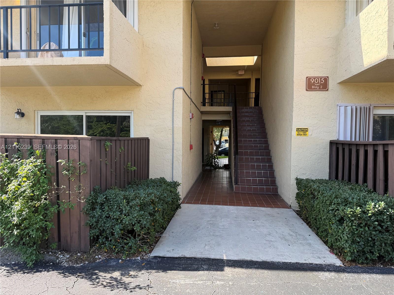 Stucco exterior featuring private balconies with metal railings, dark wood privacy fencing, a tile-paved staircase, and concrete ground-level entryway Stucco exterior featuring private balconies with metal railings, dark wood privacy fencing, a tile-paved staircase, and concrete ground-level entryway