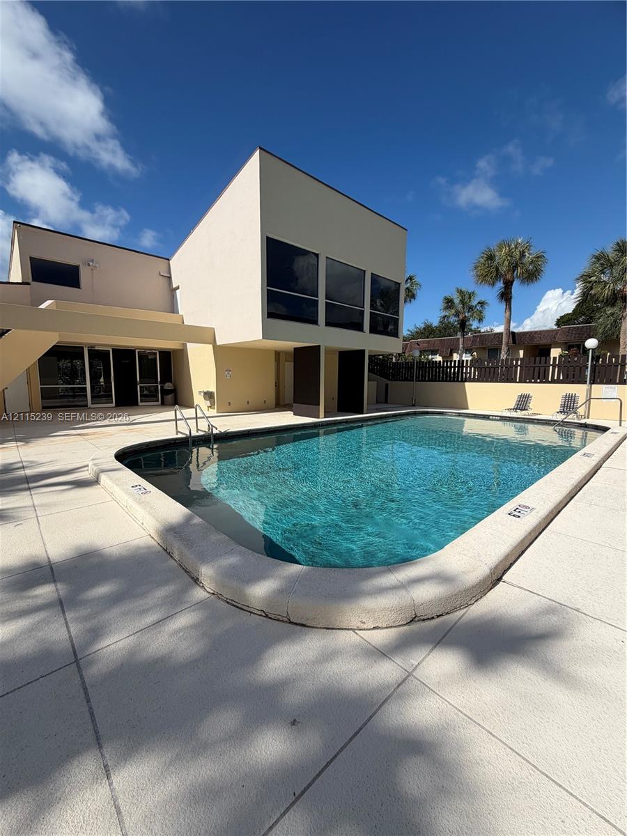 In-ground swimming pool featuring a curved concrete deck, metal pool ladder, and surrounding privacy fencing