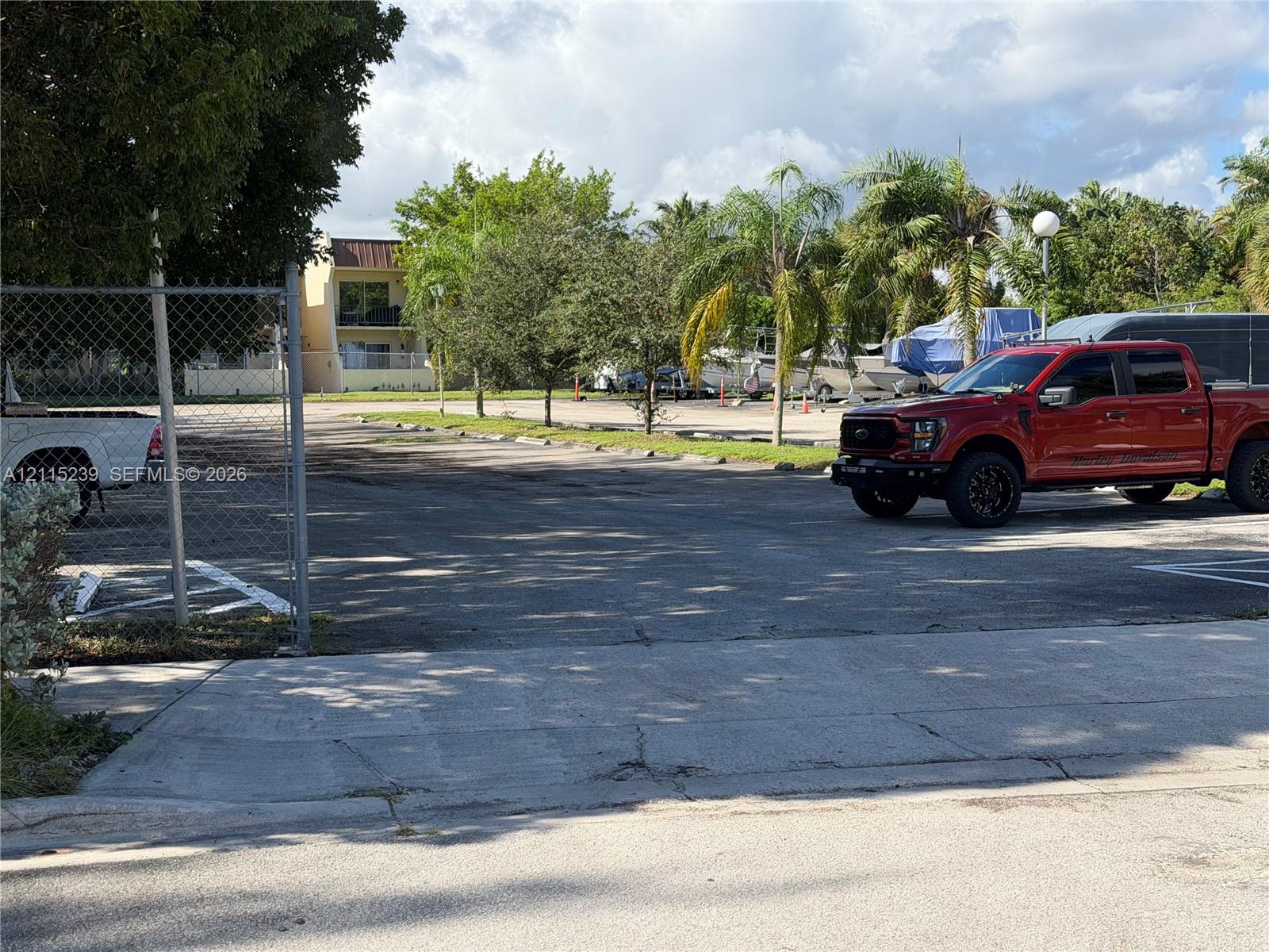 Paved surface parking lot featuring chain-link perimeter fencing and mature palm tree landscaping