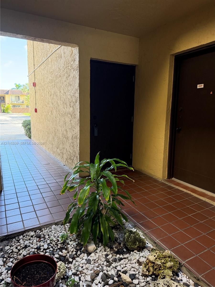 Covered exterior entryway featuring square ceramic floor tiling, stucco wall finishes, and a decorative rock landscape border Covered exterior entryway featuring square ceramic floor tiling, stucco wall finishes, and a decorative rock landscape border