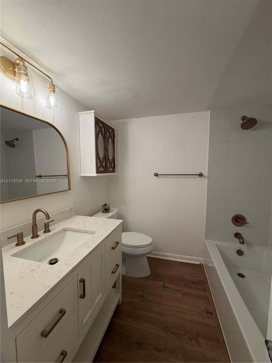 Bathroom featuring a white vanity with a stone countertop, an arched mirror, metallic fixtures, wood-finish flooring, and a shower-tub combination with tile surround