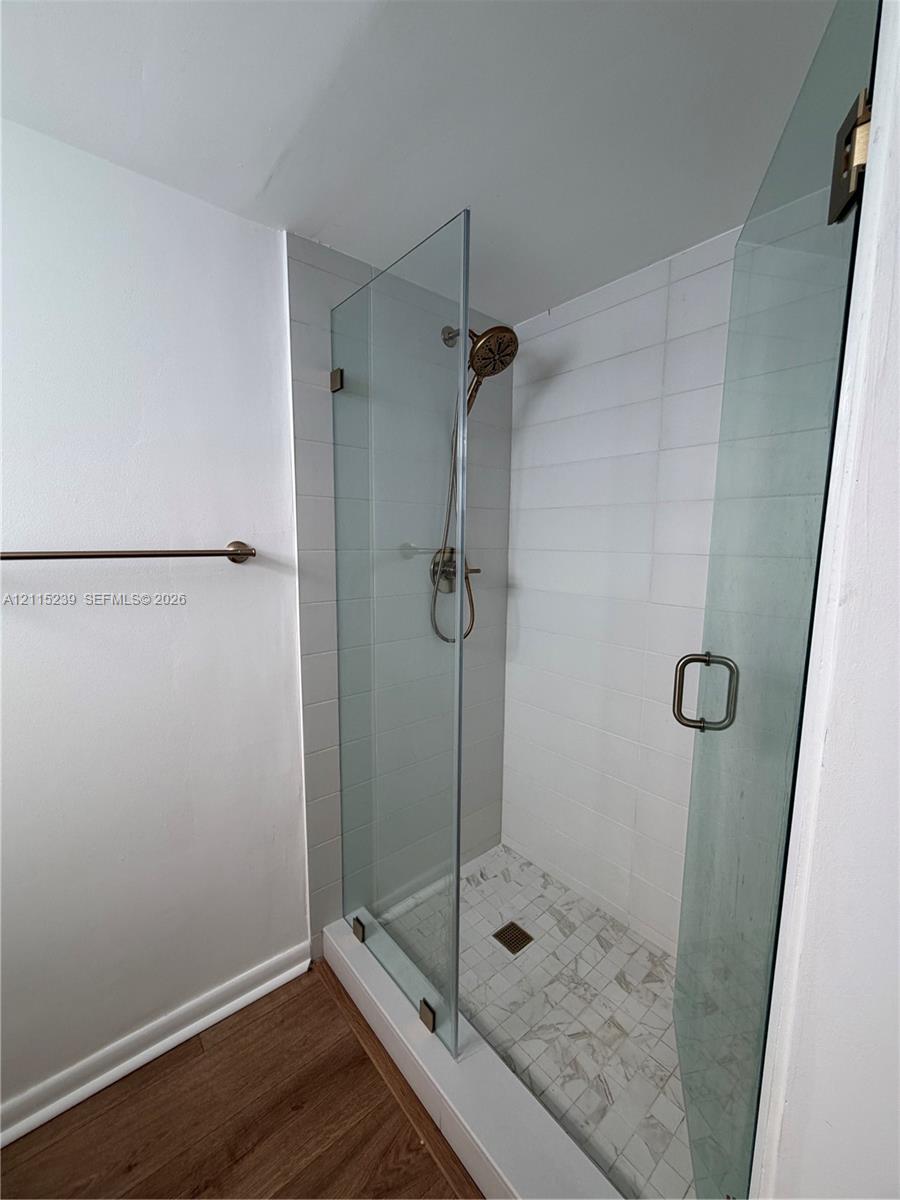 Walk-in shower featuring a frameless glass enclosure, white rectangular wall tile, stone-finish floor tile, and bronze-tone fixtures
