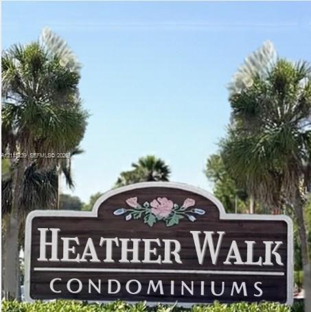 Heather Walk Condominiums entrance sign featuring a decorative floral accent, dark wood-finish background, and mature palm trees Heather Walk Condominiums entrance sign featuring a decorative floral accent, dark wood-finish background, and mature palm trees