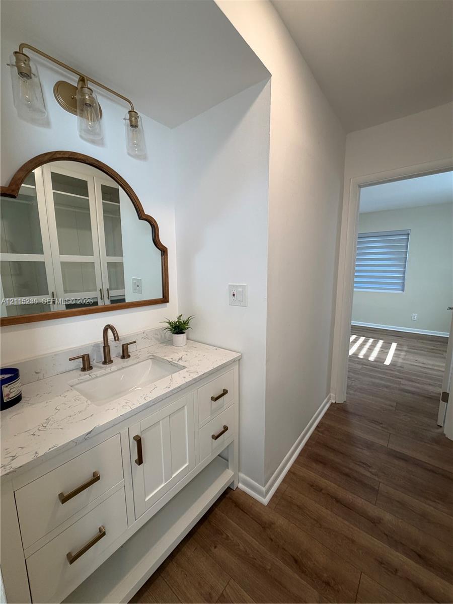 White vanity cabinet with stone countertop and integrated sink, arch-top mirror with wood frame, metallic fixtures, and overhead three-bulb vanity light