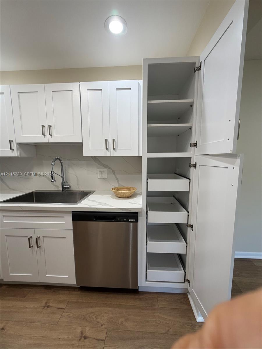 Shaker-style white cabinetry featuring a floor-to-ceiling pantry with pull-out drawers, stone-finish countertops, stainless steel undermount sink, high-arc faucet, and wood-finish flooring
