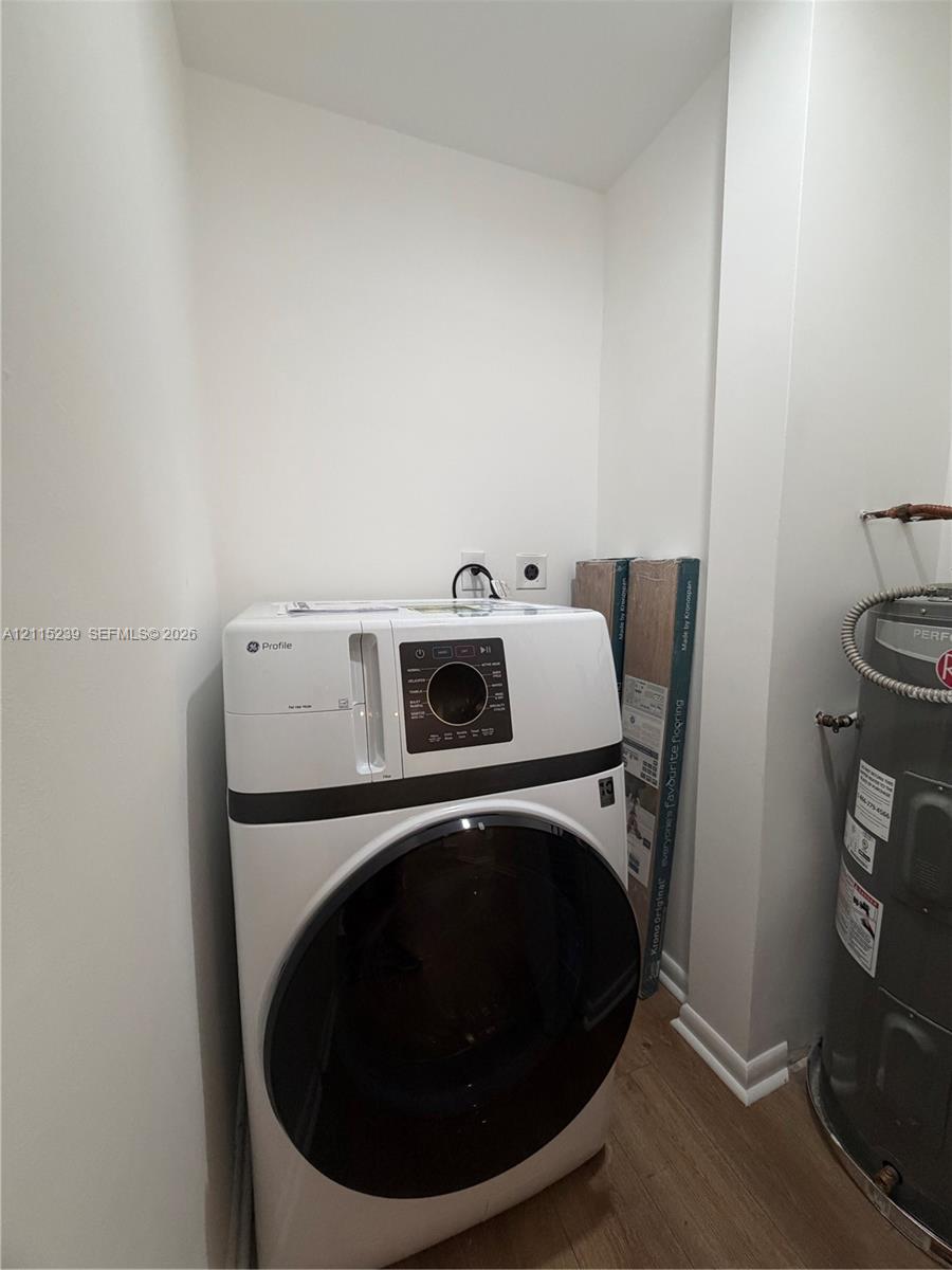 Utility area featuring wood-finish flooring, white walls, and a built-in electric water heater