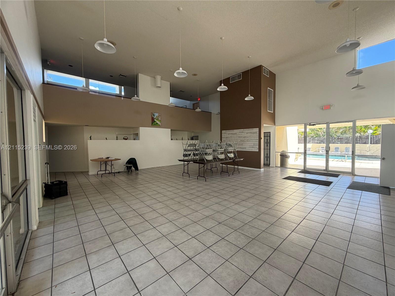 Expansive interior featuring high ceilings, ceramic tile flooring, abundant natural light from clerestory windows, and glass-paneled doors