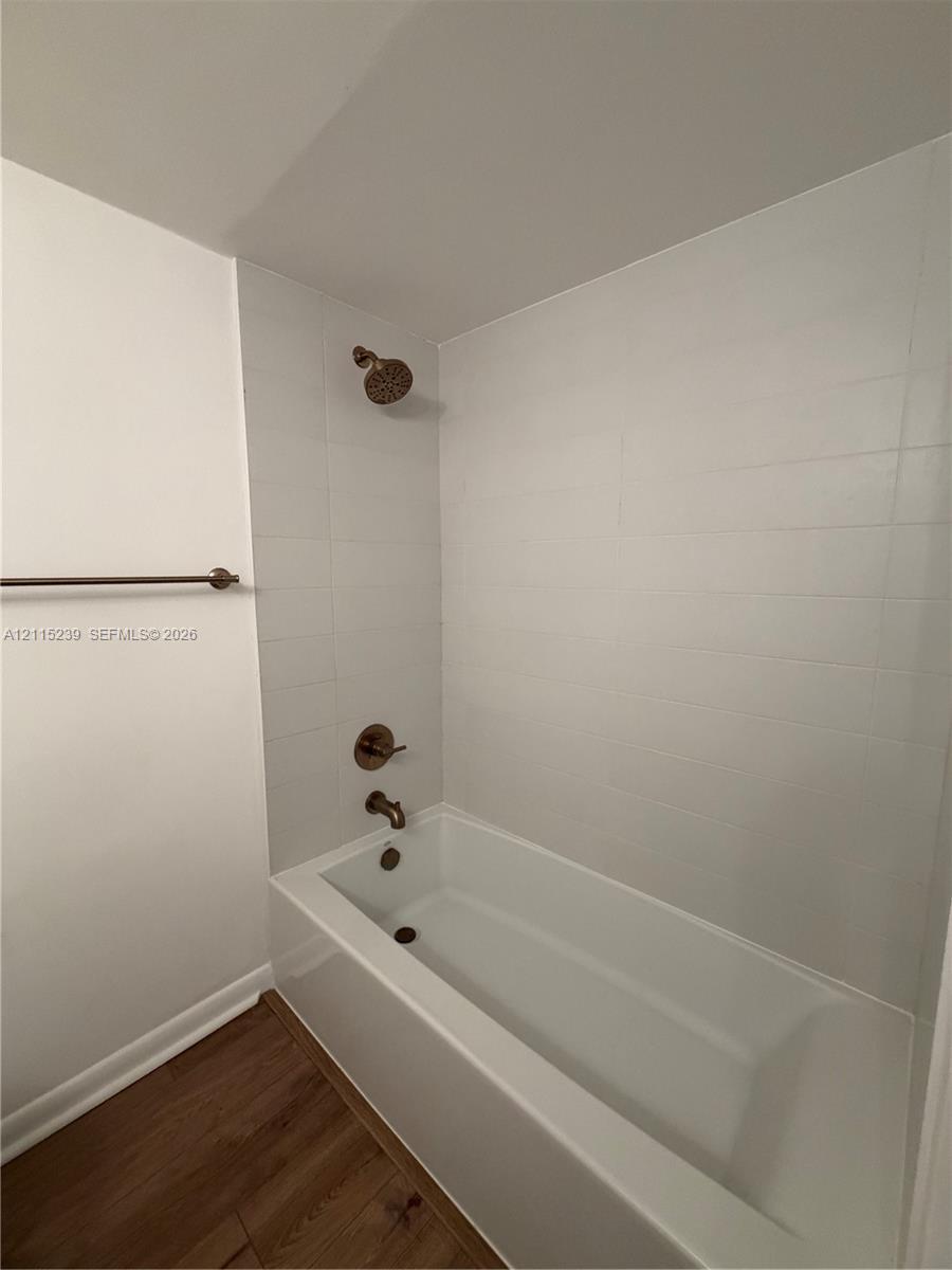 Full-size bathtub featuring white rectangular wall tile, bronze-finish fixtures, and wood-finish flooring