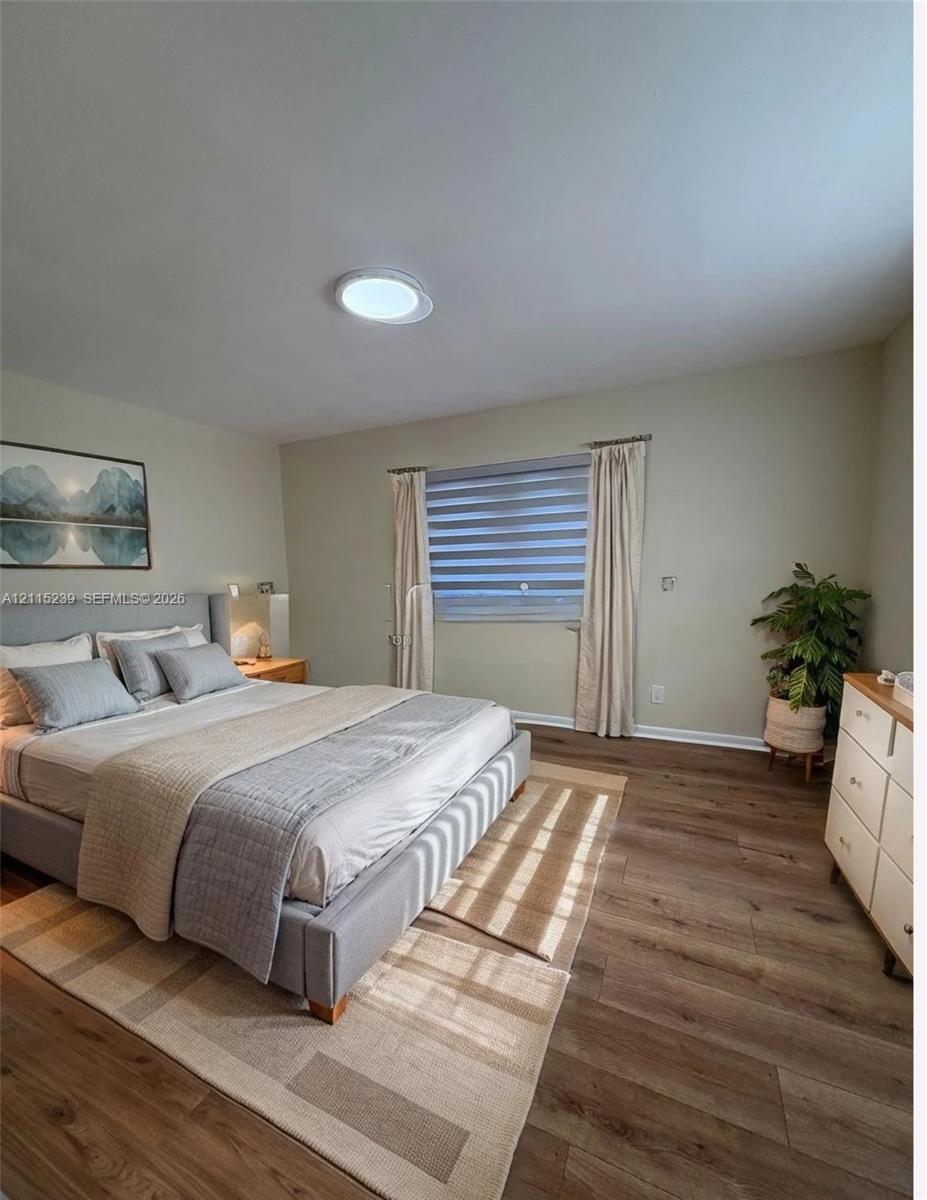 Neutral-toned interior featuring wood-finish flooring, a flush-mount ceiling light fixture, and horizontal-slat window treatments