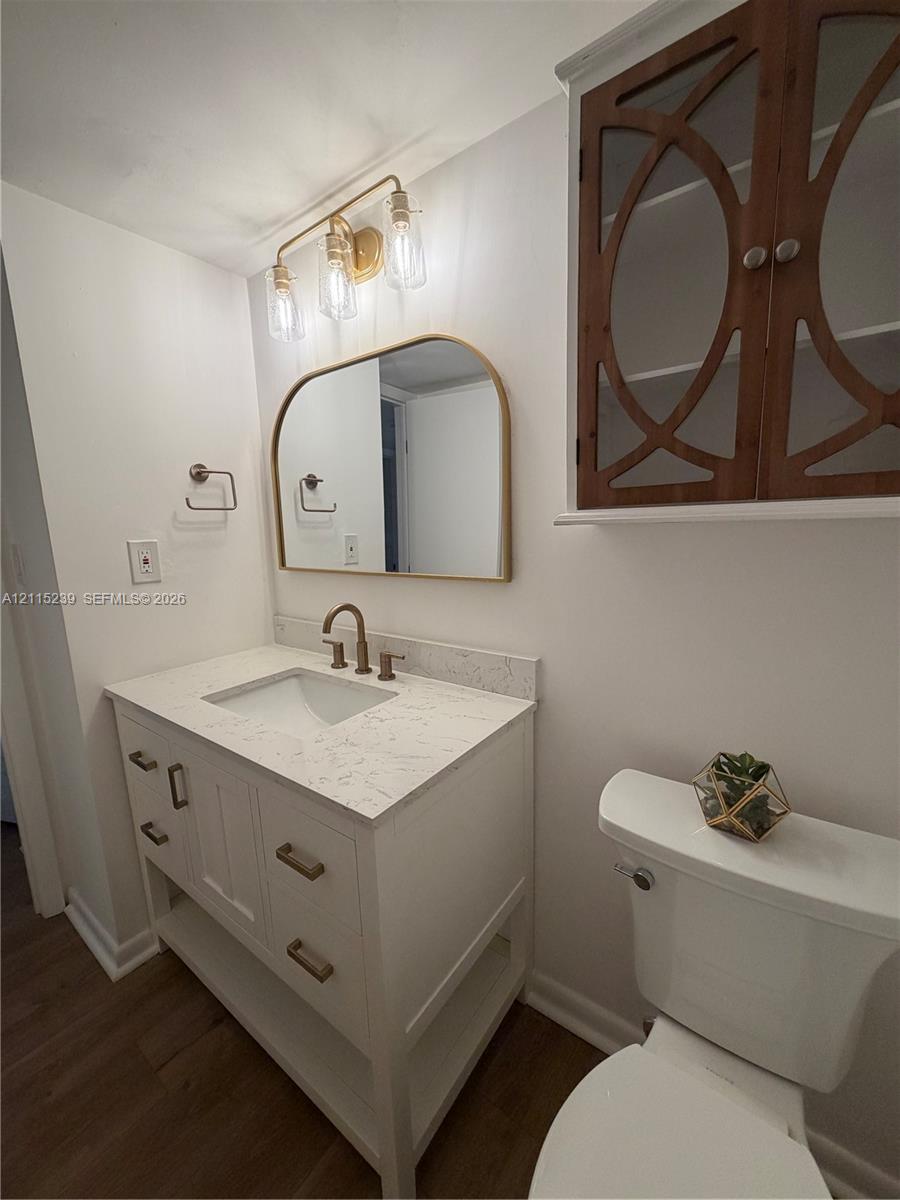 White vanity with stone-composite countertop, arched-top mirror, brass-finish fixtures, and custom-inlay wall cabinetry