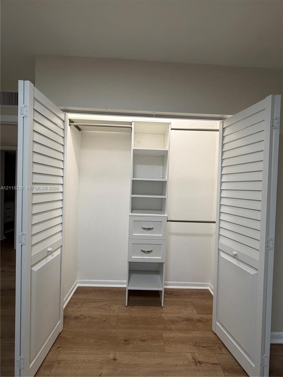 Closet featuring white louvered bifold doors, wood-finish flooring, custom built-in shelving, two integrated drawers with hardware, and dual hanging rods