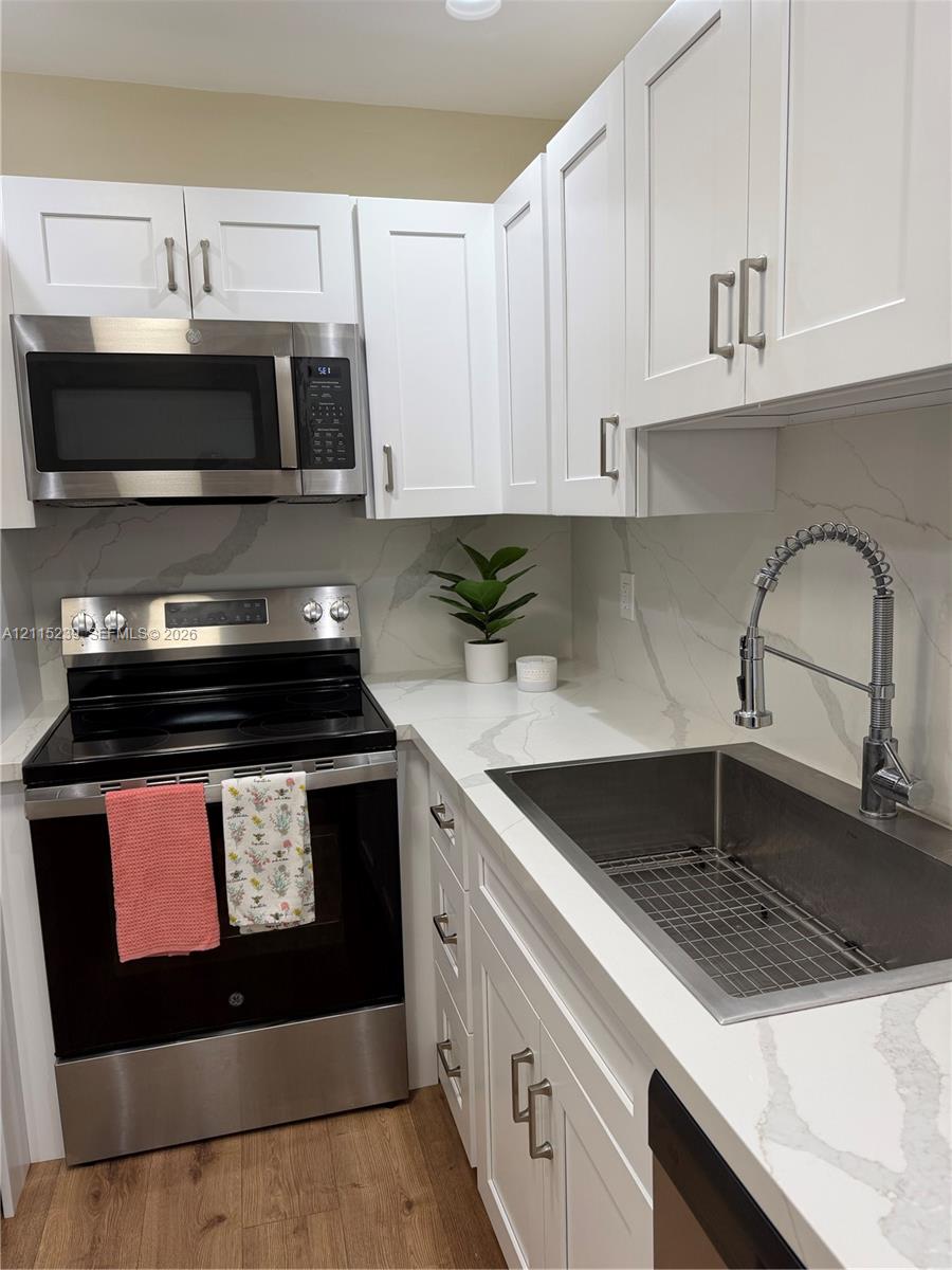Shaker-style white cabinetry, stone-finish countertops with matching backsplash, stainless steel appliances, undermount sink with high-arc pull-down faucet, and wood-finish flooring
