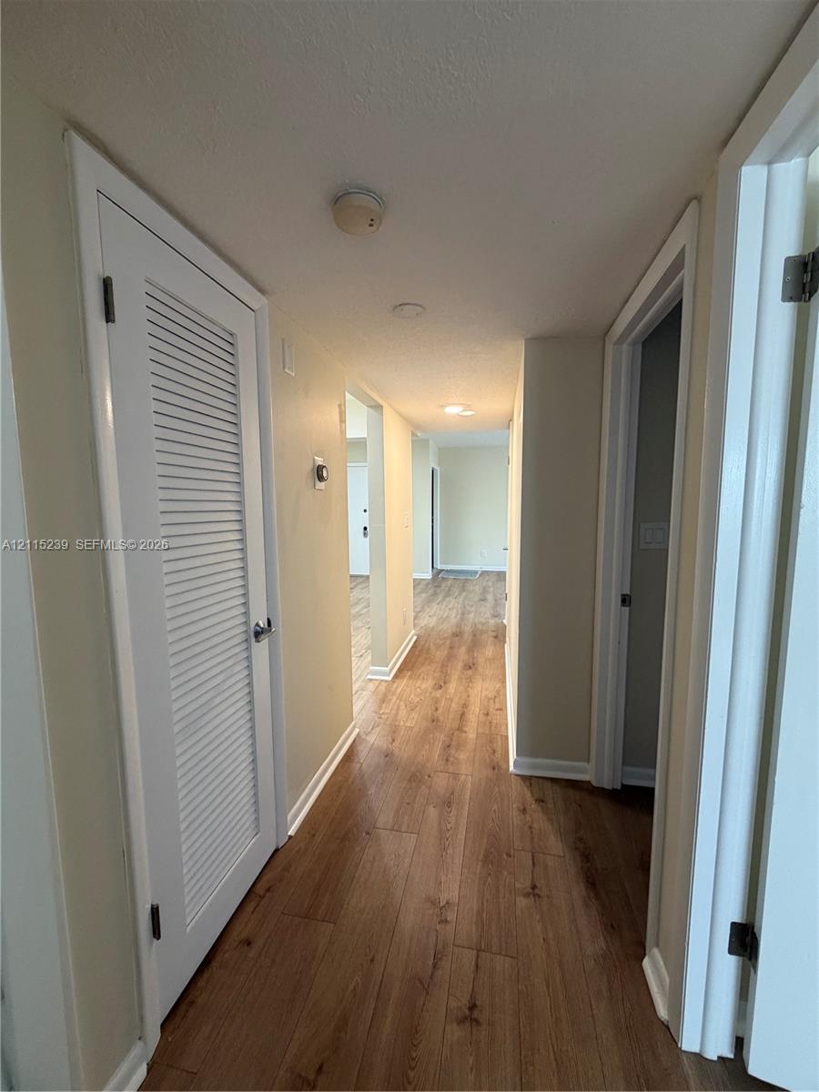 Interior hallway featuring wood-finish flooring, white louvered closet doors, and recessed ceiling lighting