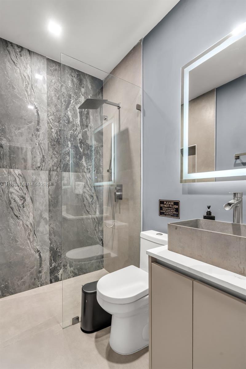 Walk-in shower with floor-to-ceiling stone-patterned tile, frameless glass panel, and rainfall showerhead