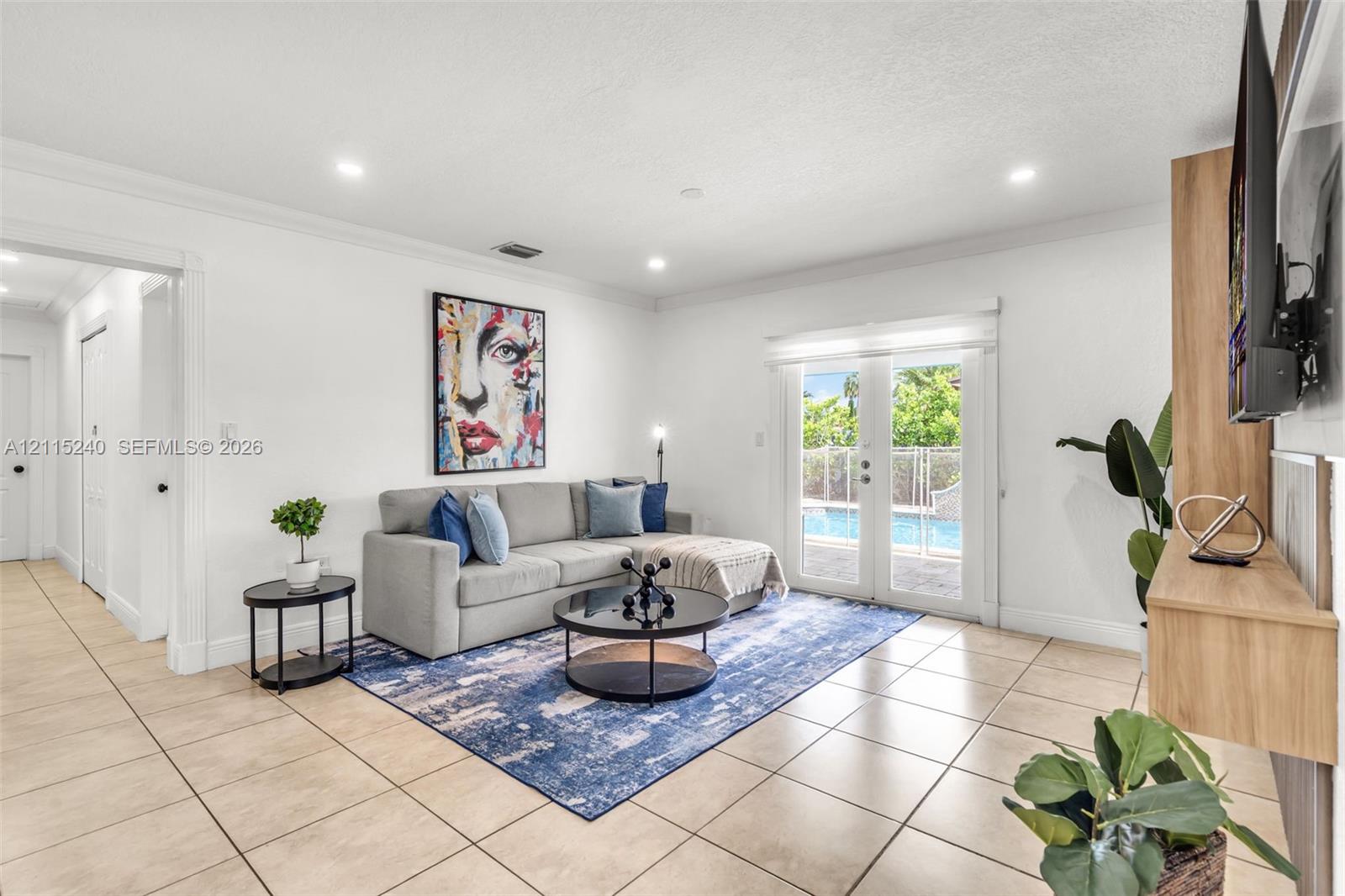 Living area featuring large-format ceramic tile flooring, crown molding, recessed lighting, a custom built-in wood-finish media console, and double glass doors providing external visibility
