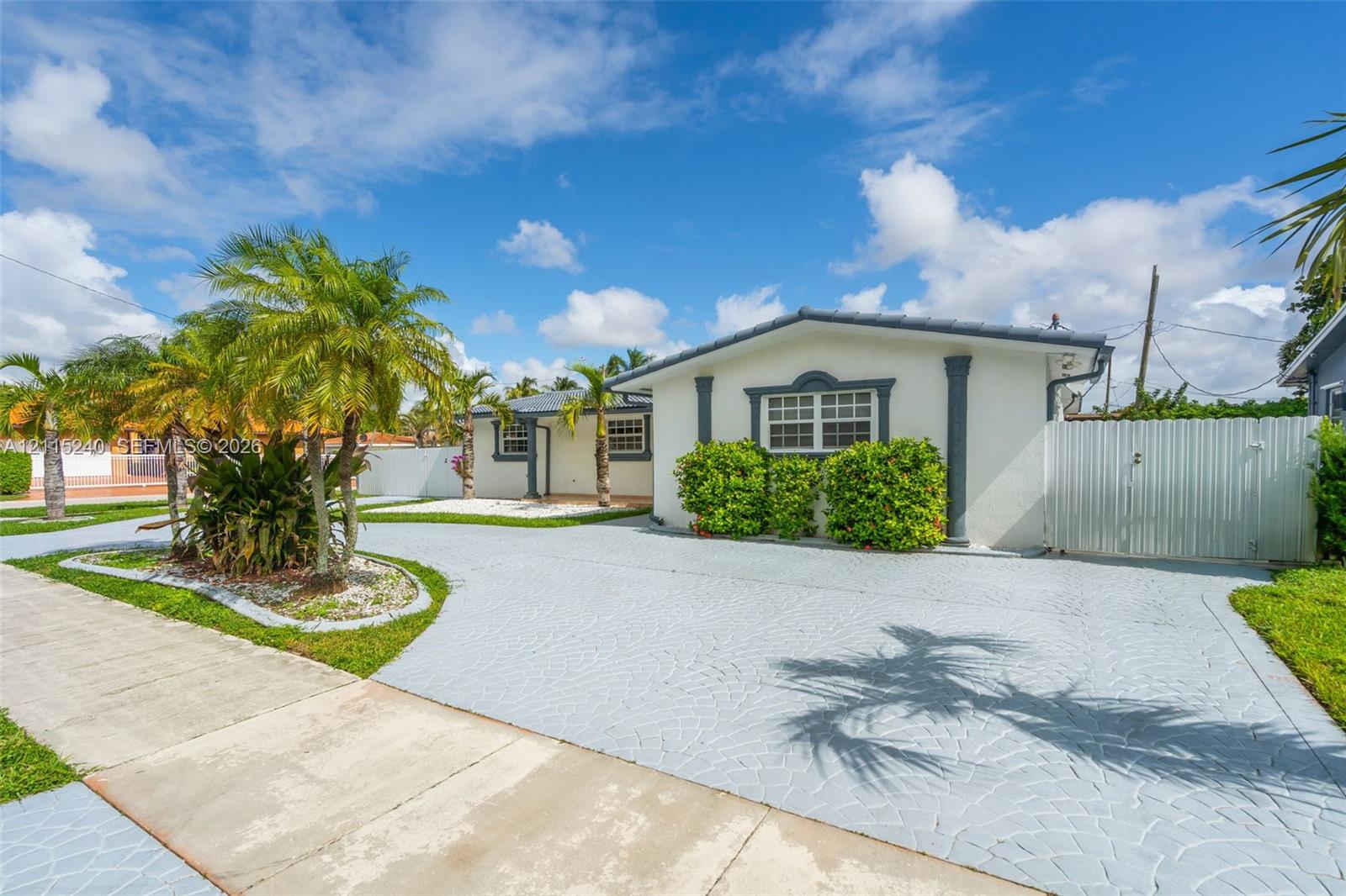 Single-story exterior featuring light-toned stucco walls, contrasting window trim, decorative columns, textured concrete driveway, and white privacy fencing