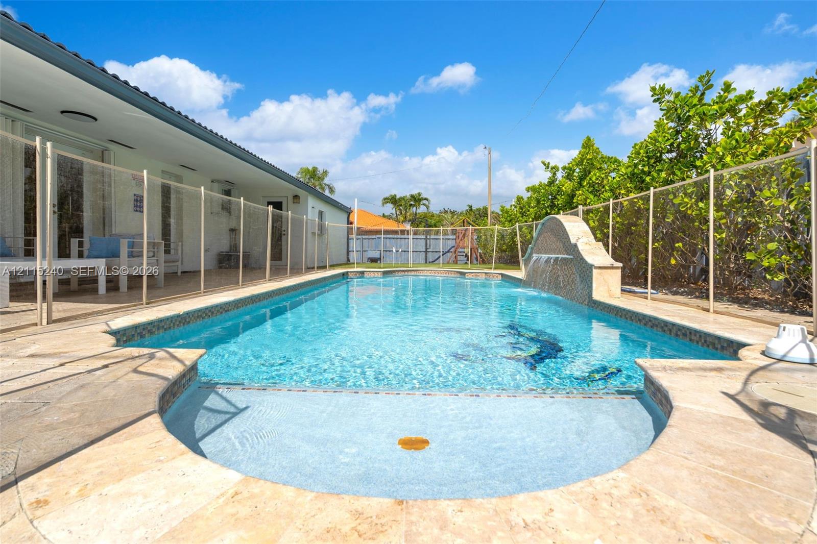 In-ground swimming pool with stone-tiled decking, integrated water feature, and a shallow sun shelf